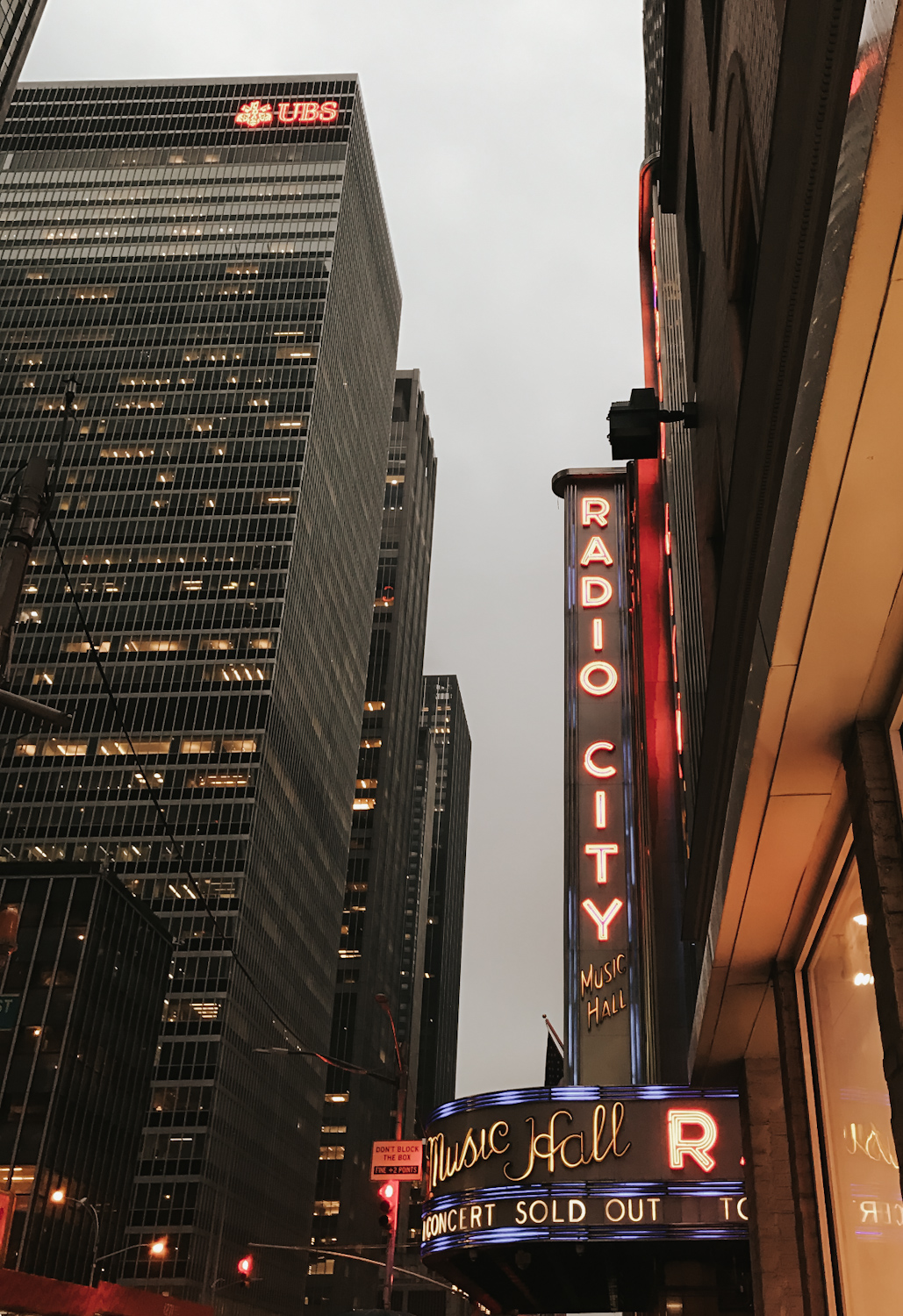 Radio City Music Hall neon marquee sign at dusk with New York City skyscrapers