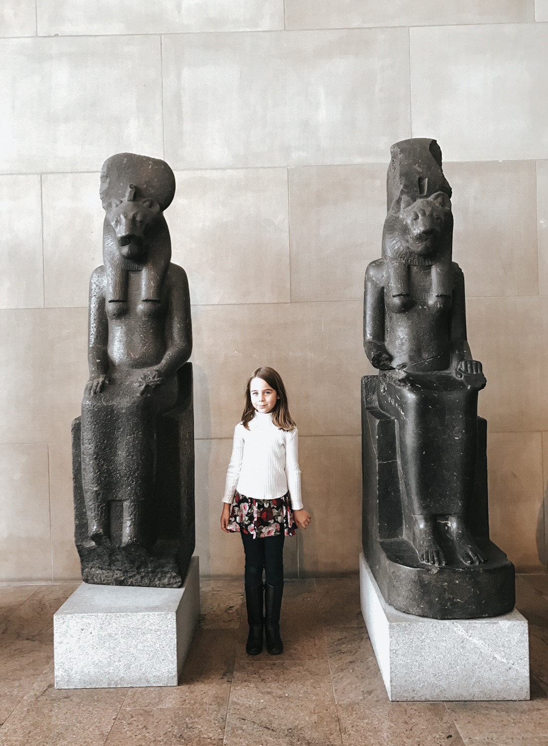 Young girl standing between two ancient Egyptian granite statues at the Metropolitan Museum of Art New York