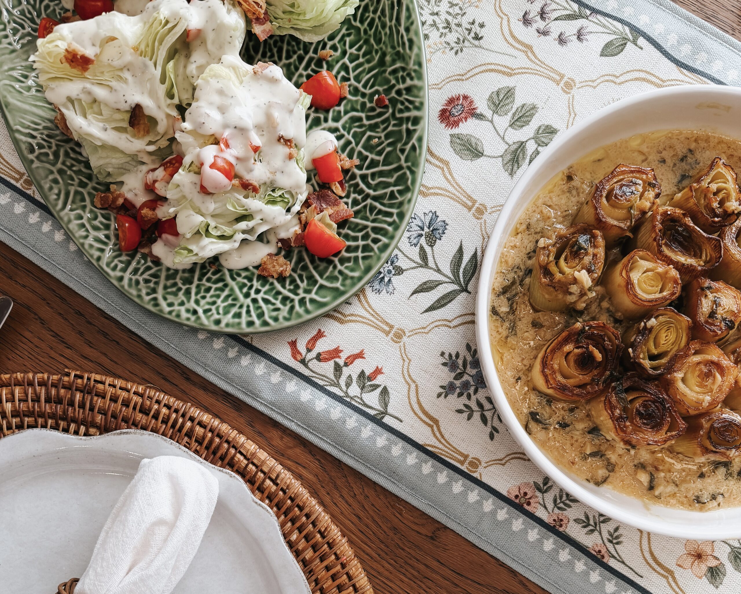 Overhead view of braised leeks in white wine sauce and wedge salad on Bordallo Pinheiro cabbage leaf platter with place setting