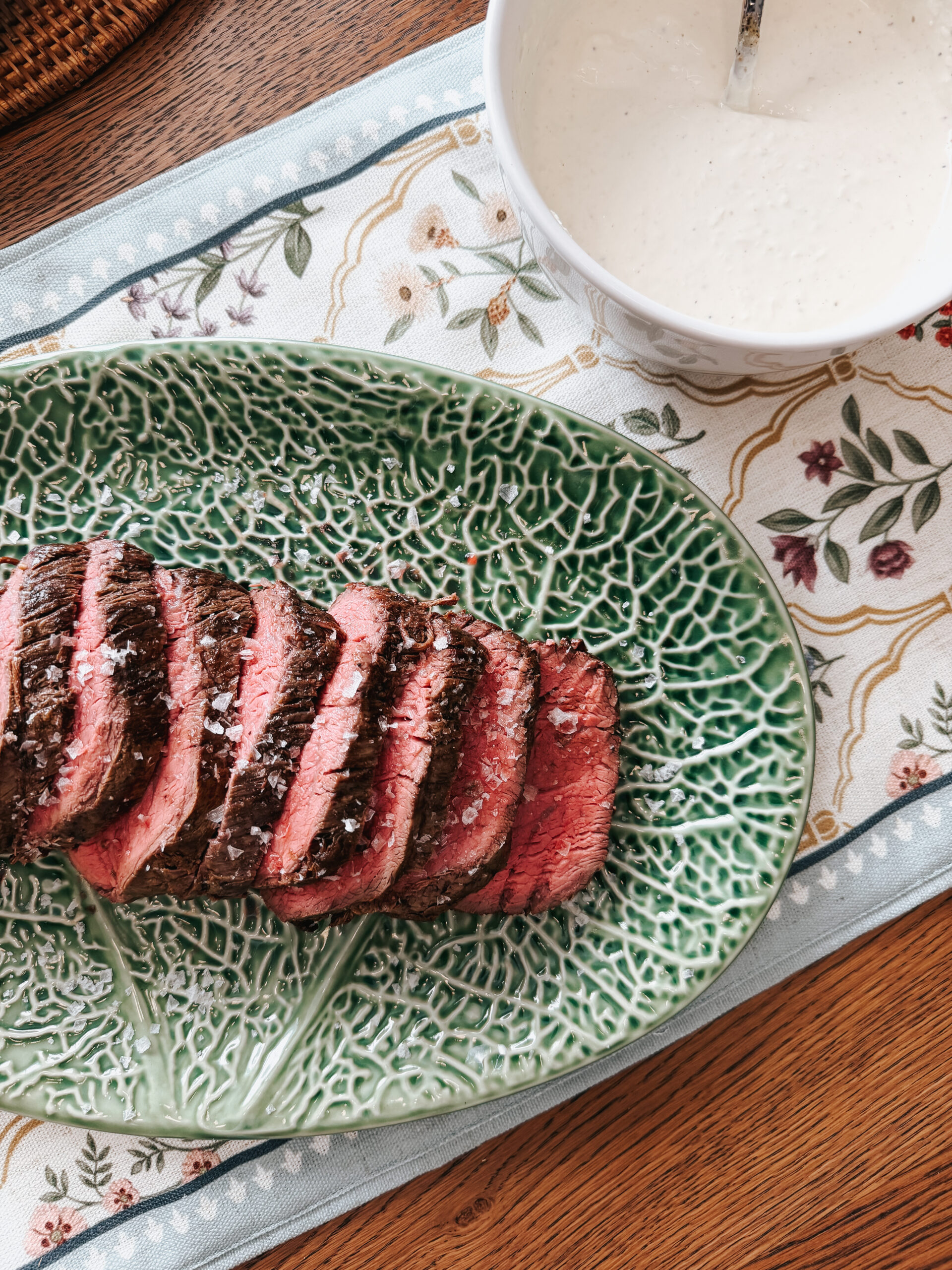 Sliced beef tenderloin with flaky salt on green serving platter with homemade horseradish cream for Easter dinner