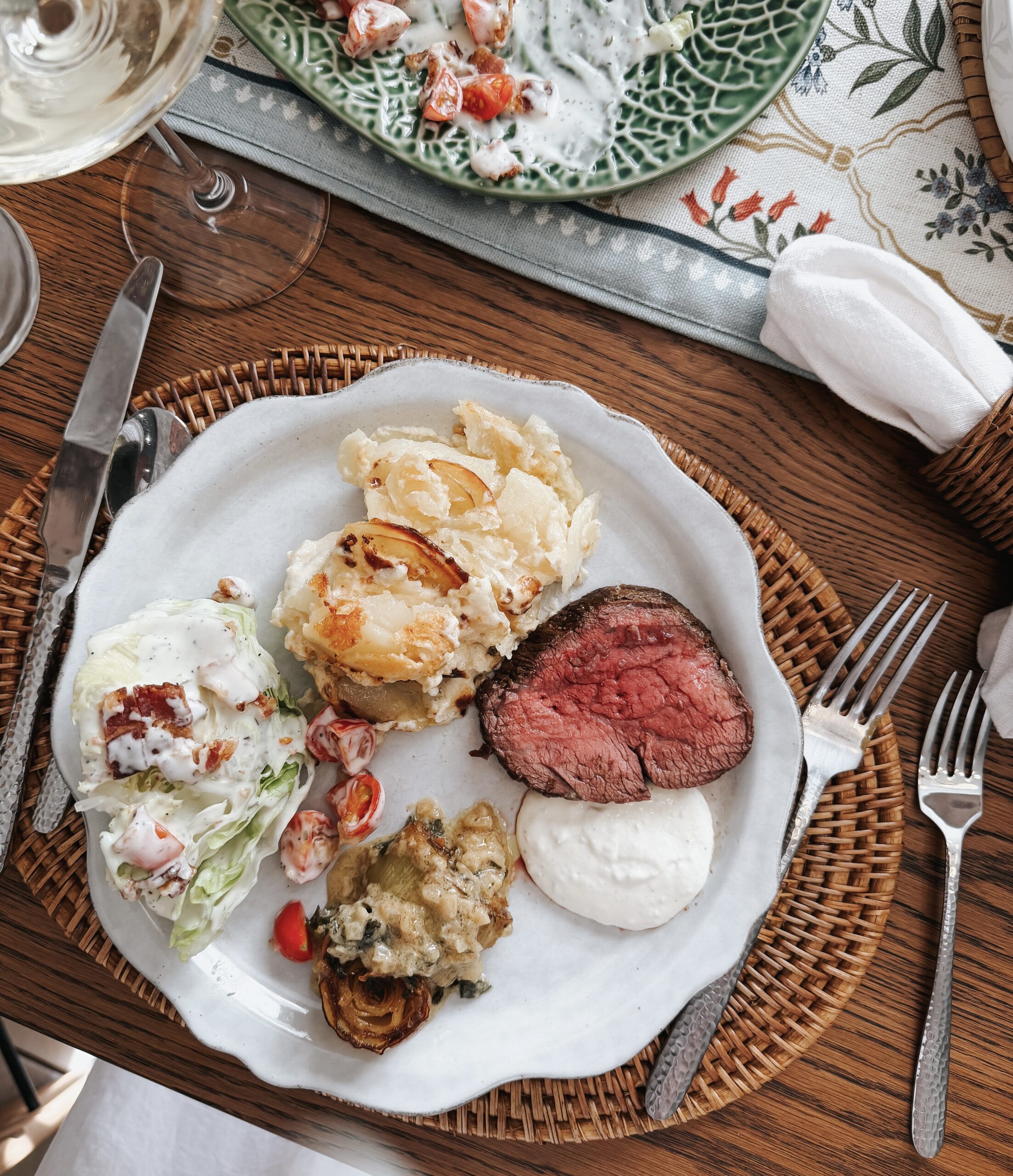 Plated Easter dinner with beef tenderloin, potatoes gratin, braised leeks, and wedge salad on scalloped white plate